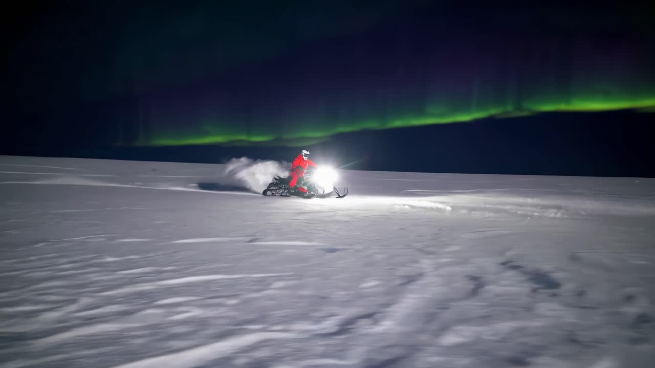 A dynamic video still of a snowmobile speeding across snowy terrain under the Northern Lights
