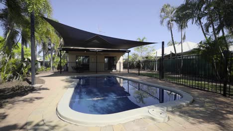 fenced pool in backyard with shade cloth on sunny day
