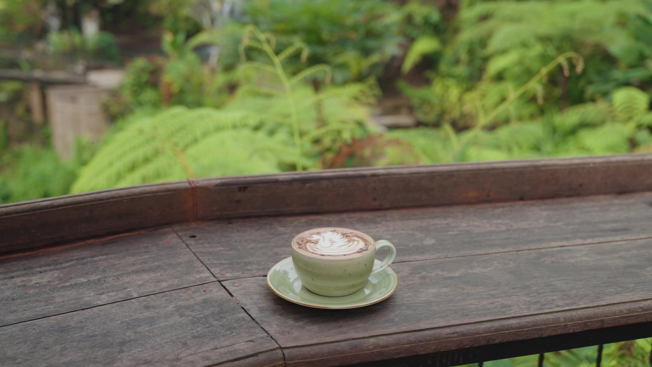 Tazza di caffè con latte art su tavolo di legno in giardino tropicale