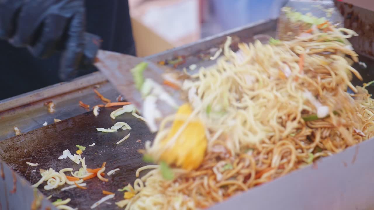 Chef adds sauce and mixes Chinese noodle dish cooking on hot grill