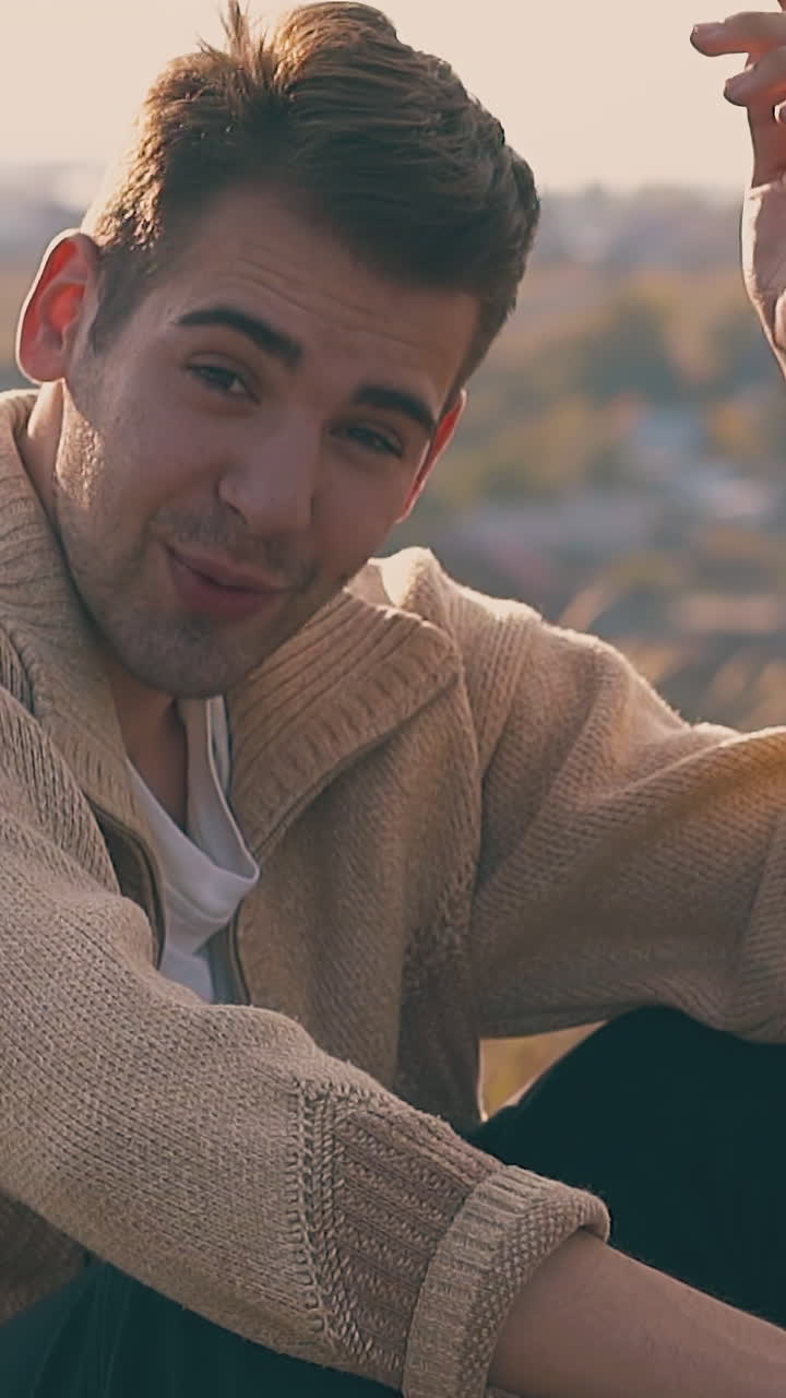 handsome guy in depression with hangover sits on river bank meadow talks holding hand on head closeup slow motion