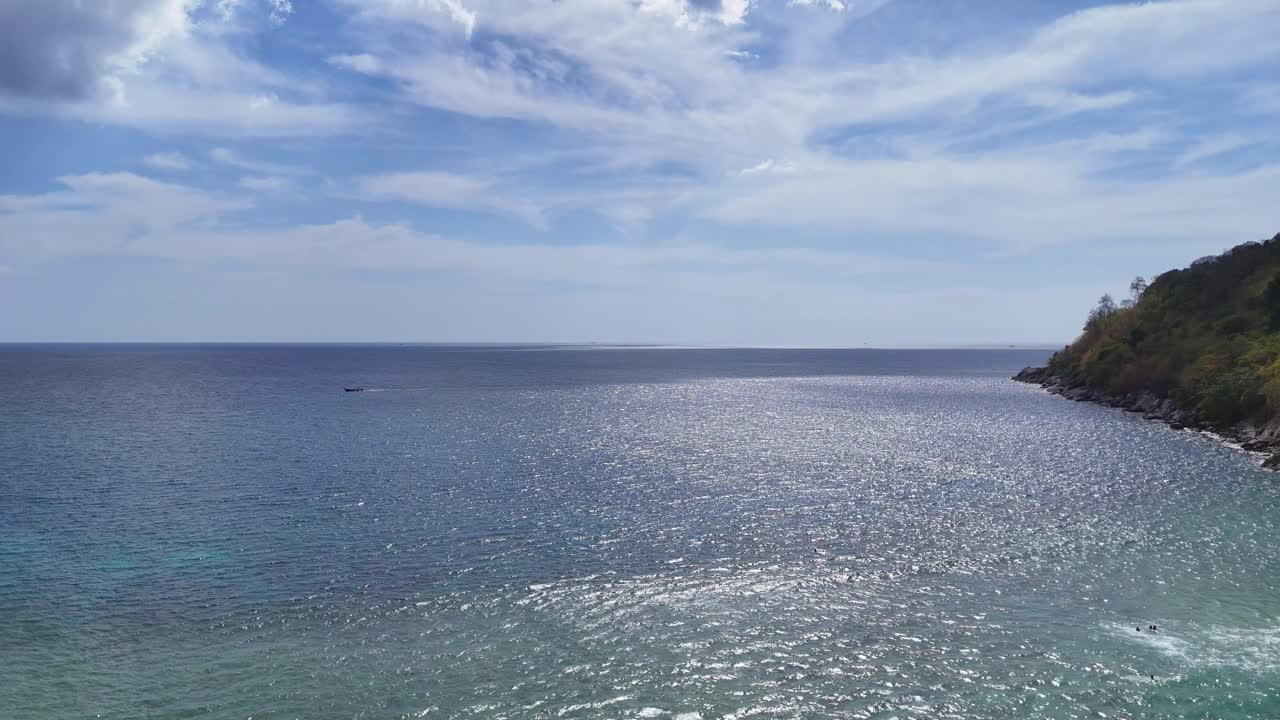 A tranquil aerial view of Phuket's coastline, showcasing calm ocean waters and lush greenery under a bright, clear sky