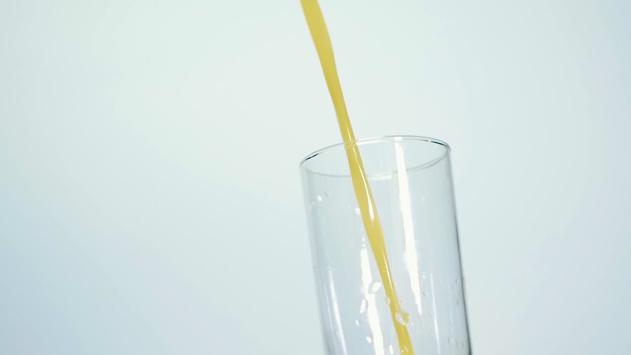 Ripresa al rallentatore di succo d'arancia fresco versato in un bicchiere su sfondo bianco. Primo piano con bassa profondità di campo.
