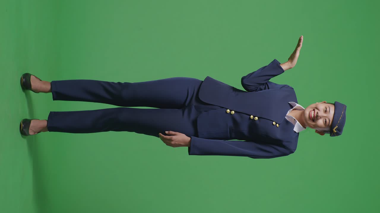 녹색 스크린 배경 스튜디오에 서 있는 동안 미소 짓고 을 가리키는 아시아 여성 에어 호스테이스의 몸이 가득 차 있습니다.