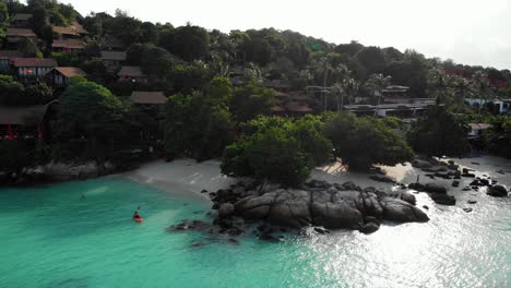 Häuser-An-Einer-Atemberaubenden-Tropischen-Küste-In-Thailand-Mit-Menschen,-Die-Im-Ozean-Kajak-Fahren-Und-Schwimmen