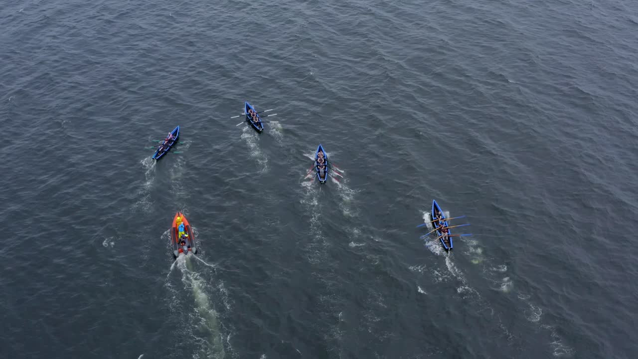 운동 선수 들 과 지원 승무원 들 은 개방 된 바다 에서 쿠라크 보트 를 빨리 오르고 있다