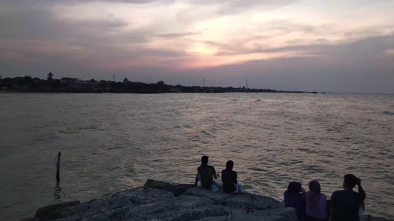 해변에서 극적인 황혼의 하늘을 즐기는 사람들