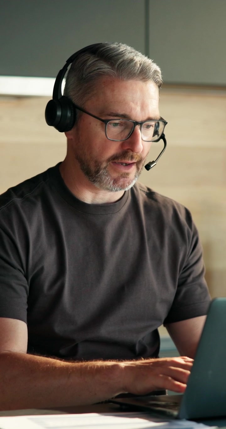 Middle-Aged Man Working on Laptop with Headset in Home Office
