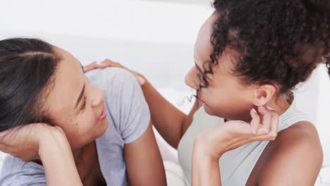 happy biracial lesbian couple lying on bed talking and embracing, in slow motion