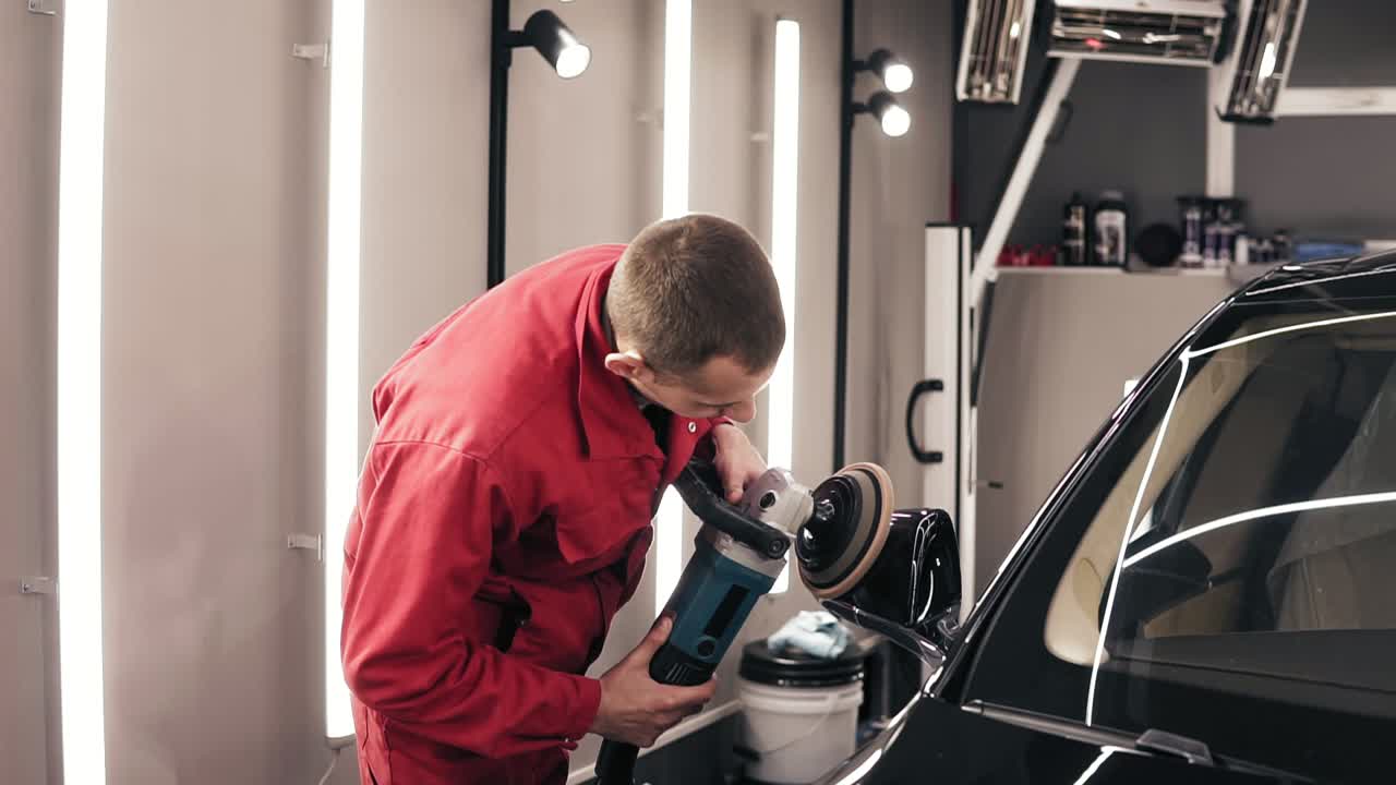 hombre en traje de trabajo rojo pulido espejo retrovisor de un coche nuevo negro.