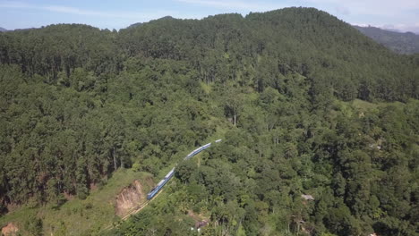 antena: tren de pasajeros serpentea a lo largo de la pista de la montaña boscosa verde