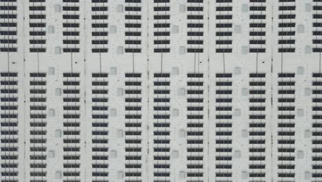 top down aerial view of hundreds of solar panels on a white roof making green renewable energy at day time on a white factory or a warehouse roof. generators, batteries and wireing visible on the side