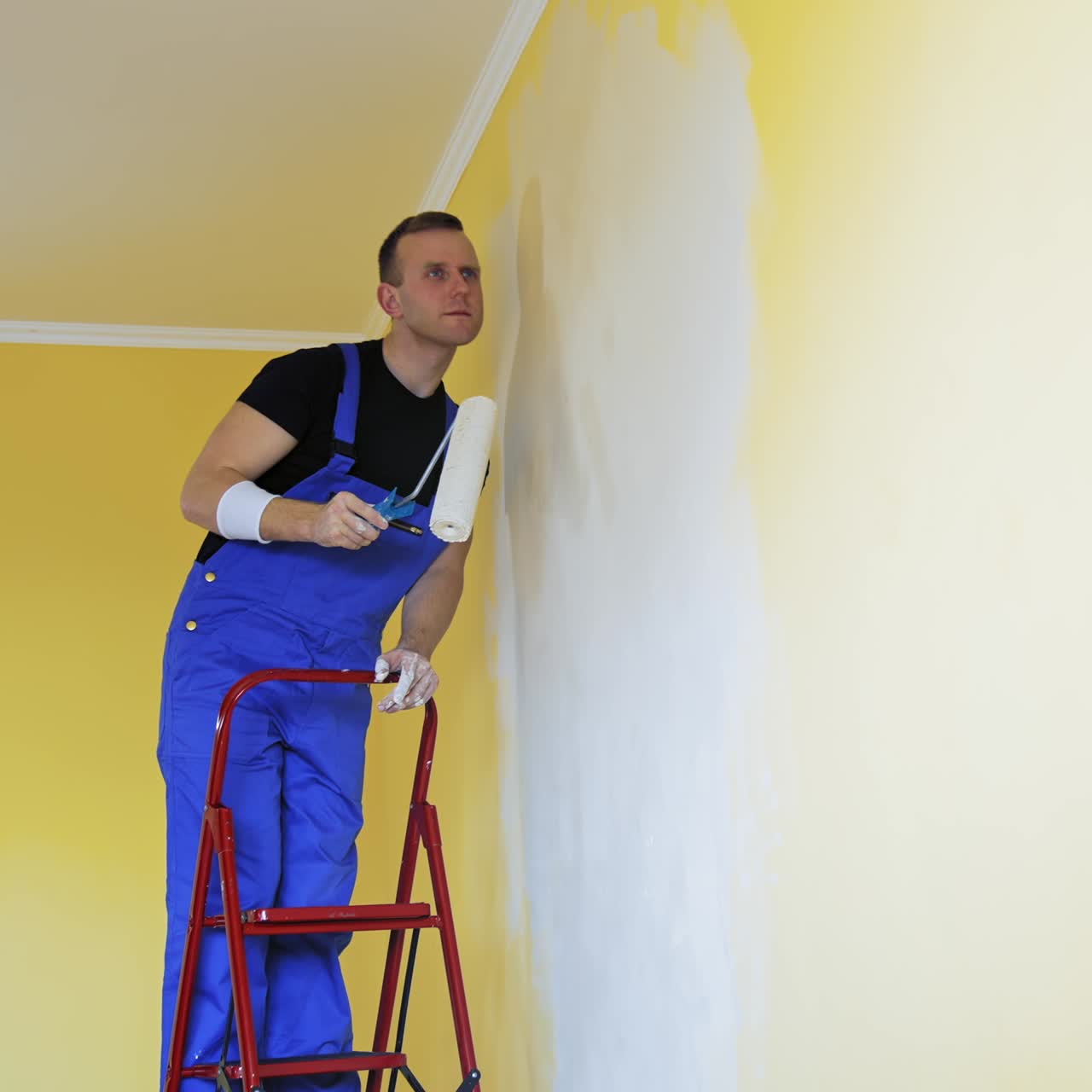 Young man in new apartment renovating room. Handsome painter working with brush roller renewing home