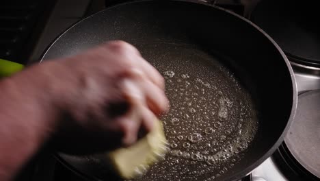 A-close-up-shot-of-a-hot-frying-pan-sizzling-and-bubbling-as-it-melts-the-end-of-a-block-of-butter-receiving-a-layer-of-grease-to-prevent-sticking,-4-eggs-are-added-to-the-pan-and-begin-cooking