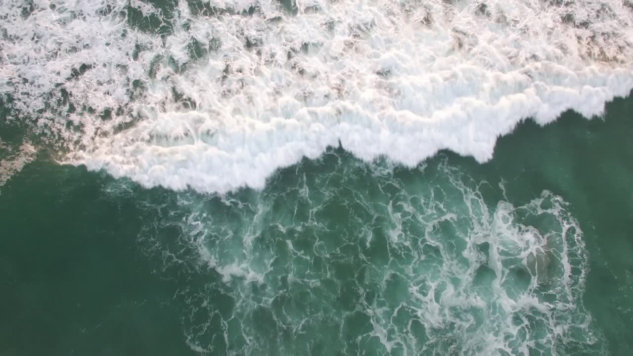 A rising aerial perspective looking straight down at the ocean with waves rolling in
