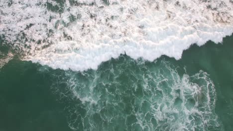 a rising aerial perspective looking straight down at the ocean with waves rolling in
