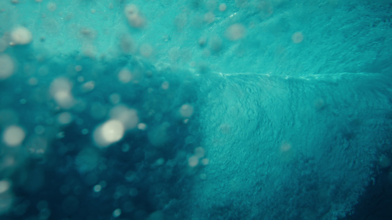 Close details of surfer riding down the line of ocean surface and breaking wave with splashing water droplets, abstract underwater pov