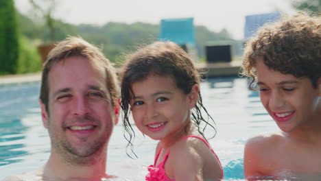 portrait of multi-racial family relaxing in swimming pool on summer vacation together