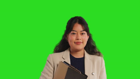 retrato de estudio en primer plano de una maestra o mujer de negocios de pie contra una pantalla verde llevando una carpeta