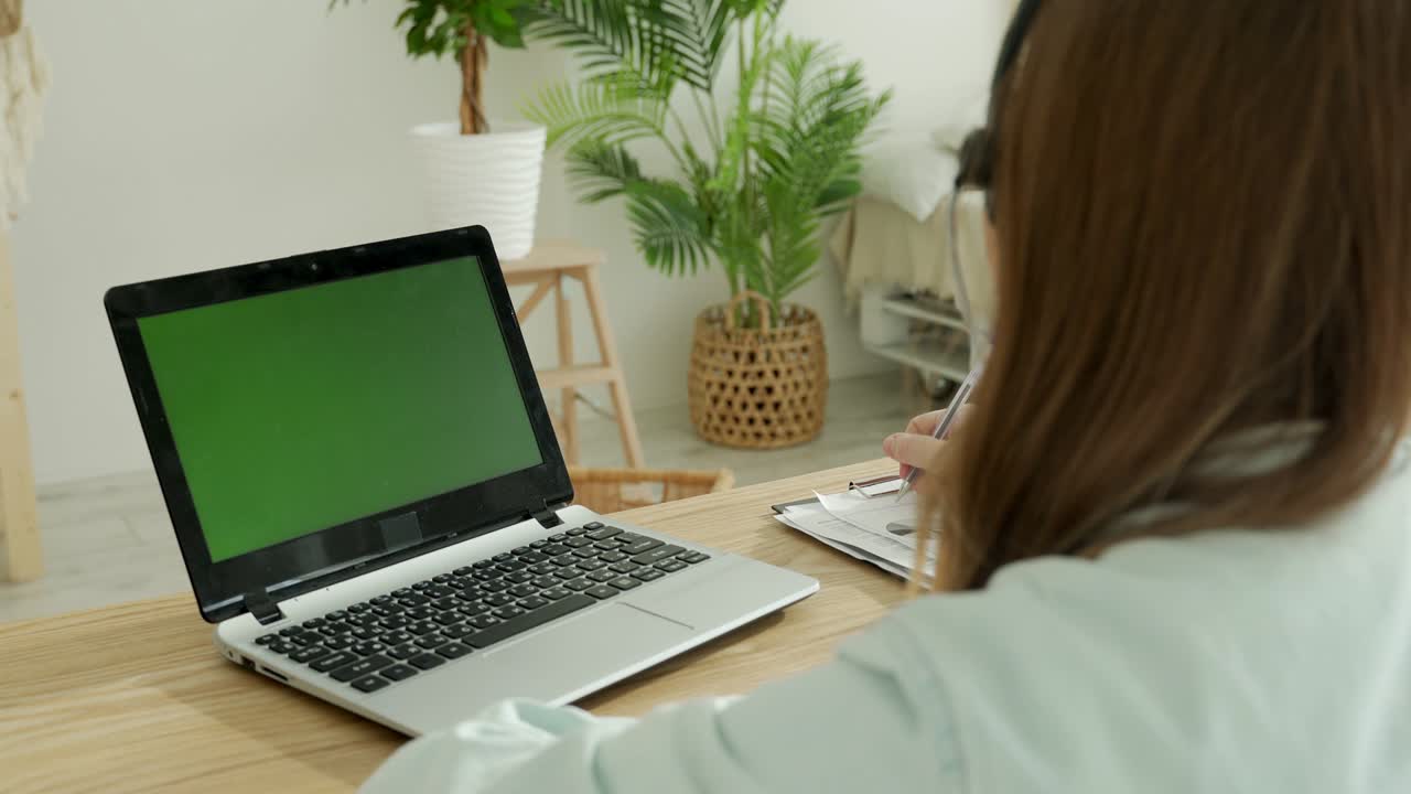 una mujer joven con auriculares haciendo una llamada de video frente al monitor.