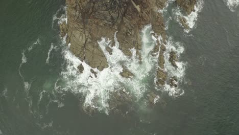 Aerial-zoom-in-of-waves-breaking-and-swelling-against-rocky-outcrop