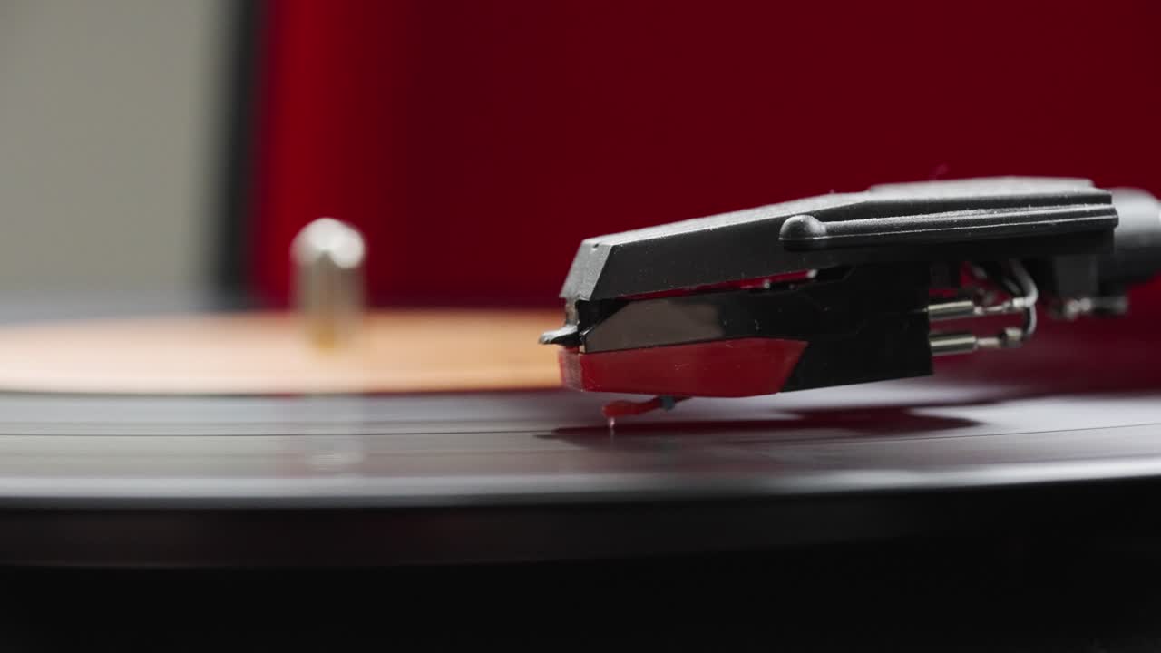 Macro view with a record needle touching black vinyl playing on a vintage red record player