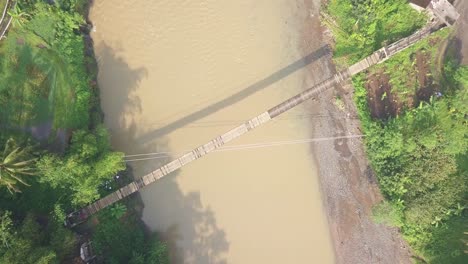 Toma-Aérea-De-Arriba-Hacia-Abajo-De-La-Motocicleta-Que-Cruza-El-Puente-Colgante-Durante-La-Mañana-Nublada-En-Java-Central,-Indonesia