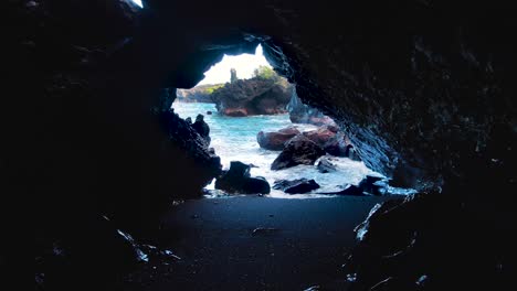 cueva volcánica con vistas a la playa de arena negra, olas del océano salpicando las rocas de la costa, parque estatal de waianapanapa