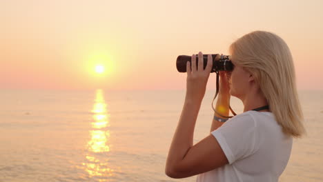 attractive young woman looks through binoculars at sunrise over the sea romance and adventure 4k vid