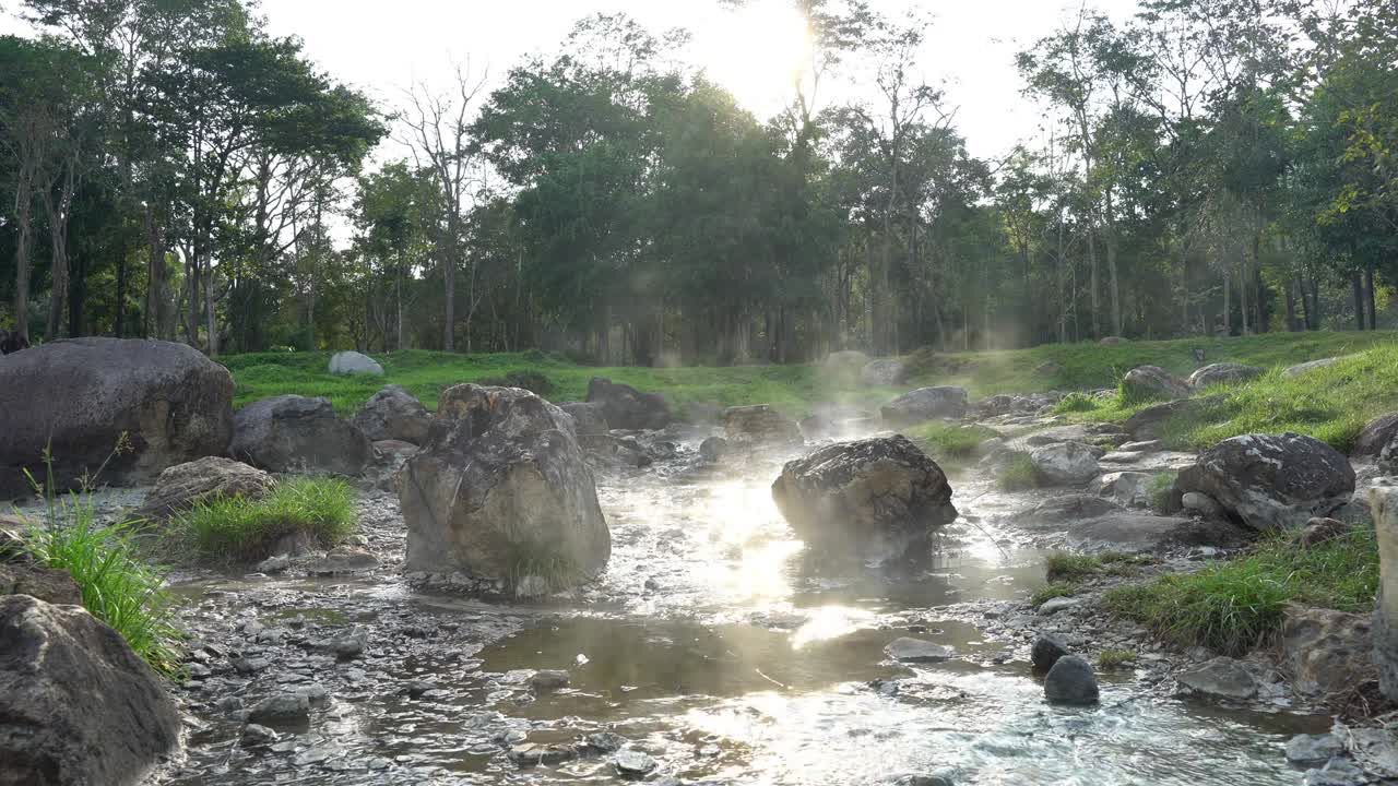 자연 온천에서 아져 나온 천천히 는 4k는 저녁의 빛 반사 아래 바위를 따라 흐르고, 불과 함께 증기가 나무와 풀의 배경으로 떠다니고 있습니다.