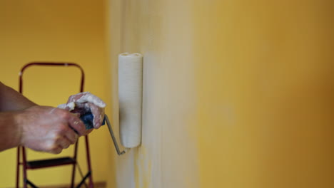 hand with paint roller during room renovation. man moving paint roller with white color on the wall. professional painting services. close-up.