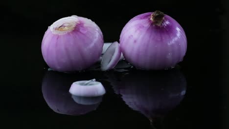 whole red onions in puddle of water with slices of onion rings falling in slow motion