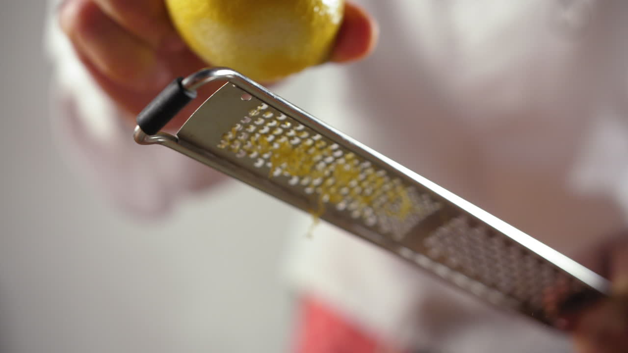 Close Up Shot of a Professional Chef Grating Lemon on a dish, slow motion shot, blurred white background