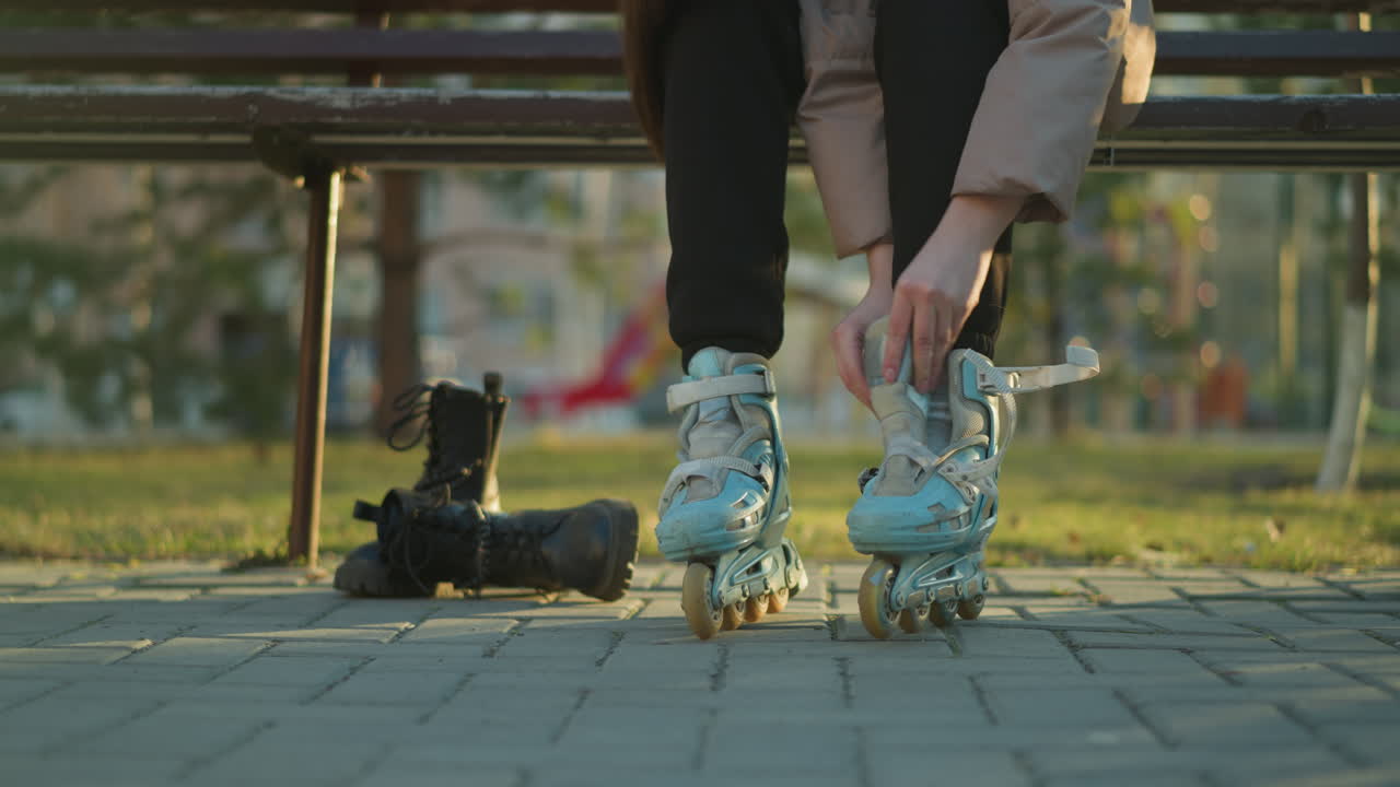 una toma de primer plano de una persona sentada en un banco del parque, atando las correas de un patineta en un pie mientras el otro pie ya está en un patinete. la persona no es completamente visible