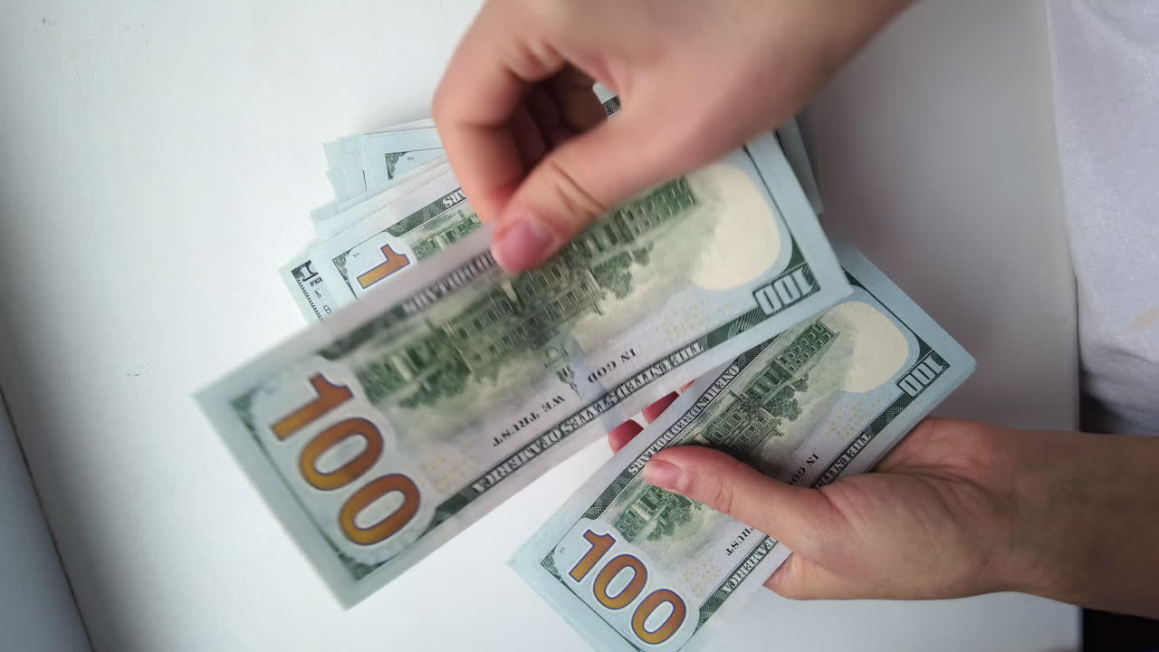 Hands are counting and sorting several stacks of hundred-dollar bills in a clean, bright space at a financial center. Attention to detail is evident in each movement