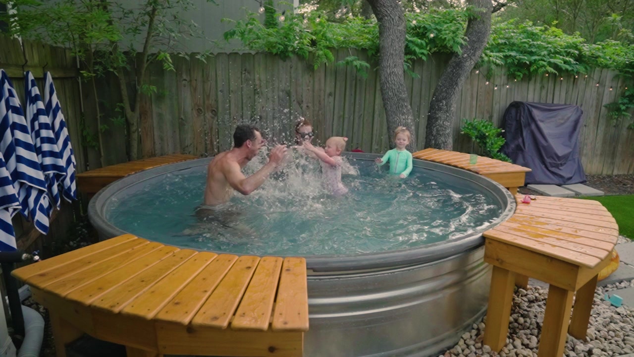 Famiglia di quattro persone che sguazza con grandi schizzi in una piscina stocktank in giardino, con l'acqua che vola, vacanza estiva al rallentatore in 4k. Annunci di lifestyle familiare, contenuti di divertimento estivo e spot pubblicitari per giornate in piscina