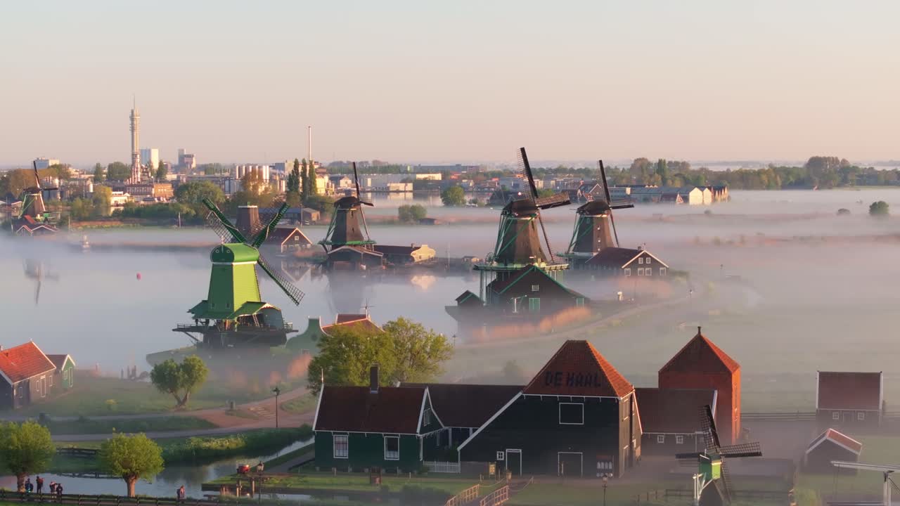 Luftaufnahme von nebelverhangenen Windmühlen und einem ruhigen Kanal bei Sonnenaufgang in Zaanse Schans.