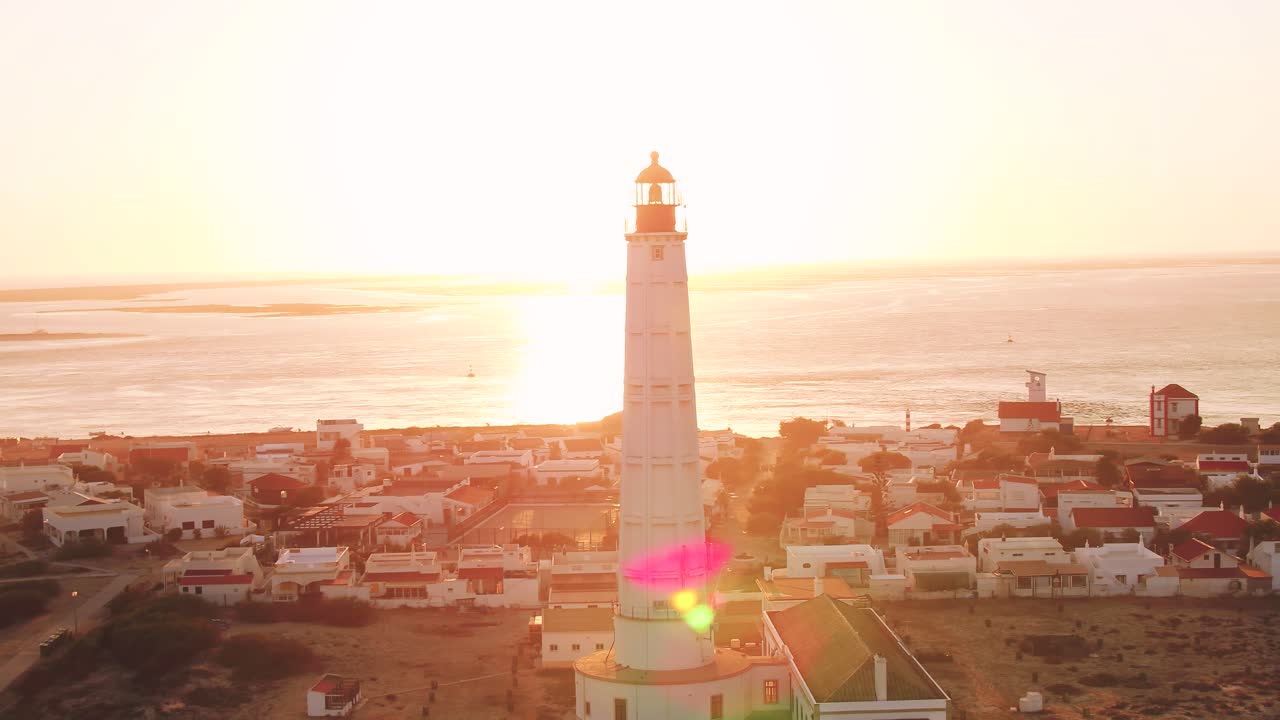 Cabo de santa maria lighthouse on Ilha do Farol. Cinematic aerial shot panning around the structure revealing the glorious sunset out at sea