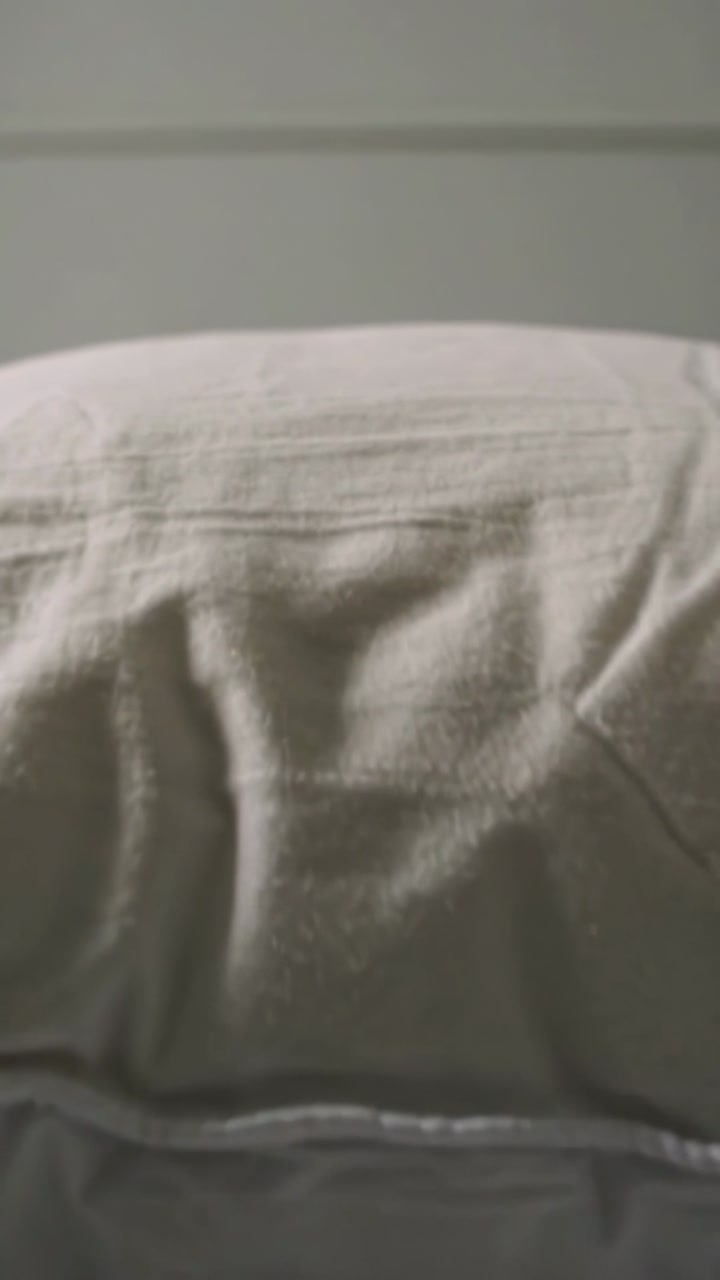 Vertical video: Pulling back camera revealing textured pillow on mattress in bedroom, showing seam