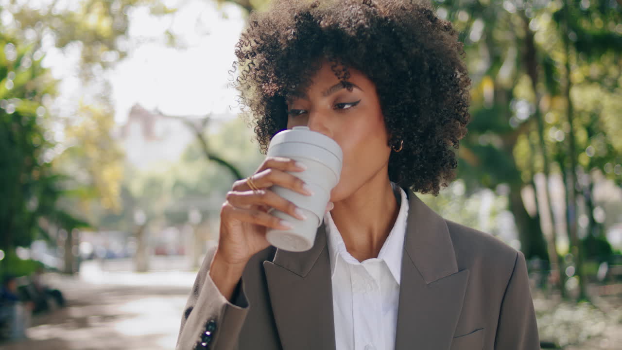 mujer africana bebiendo café de pie en el parque de la ciudad de primer plano. niña disfrutando de la bebida