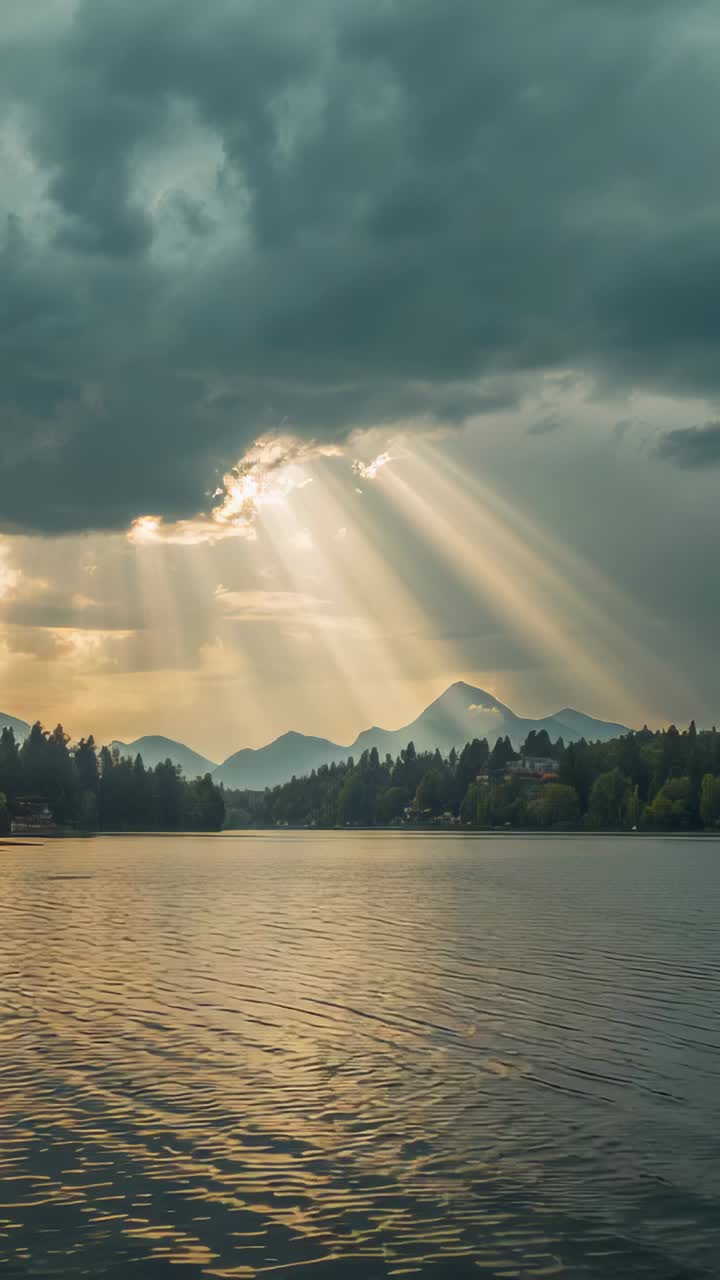 Vertical video: Piercing rays sweeping from cloud gap opening over mountains, reflecting on lake