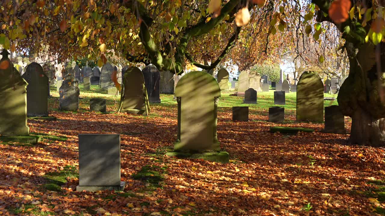 Old gravestones with moss and orange leaves in quiet British cemetery
