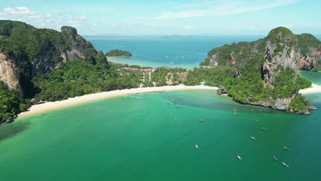 aerial view showing tropical railay beach with arriving boats during sunny day - beautiful panorama view with green mountains and ocean in background