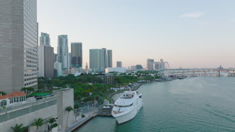 Pull-back-shot-of-boat-mooring-at-bank-in-city.-Revealing-panoramic-view-of-modern-urban-borough-and-bridge-over-sea-bay.-Miami,-USA
