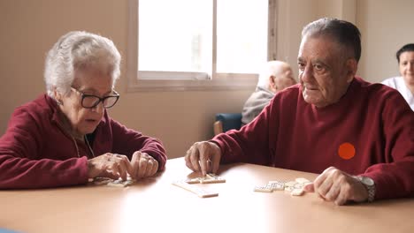 senior friends playing dominoes at table in nursing home
