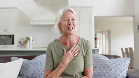 Happy-caucasian-senior-woman-having-video-call-and-waving-hand-in-sunny-living-room,-slow-motion