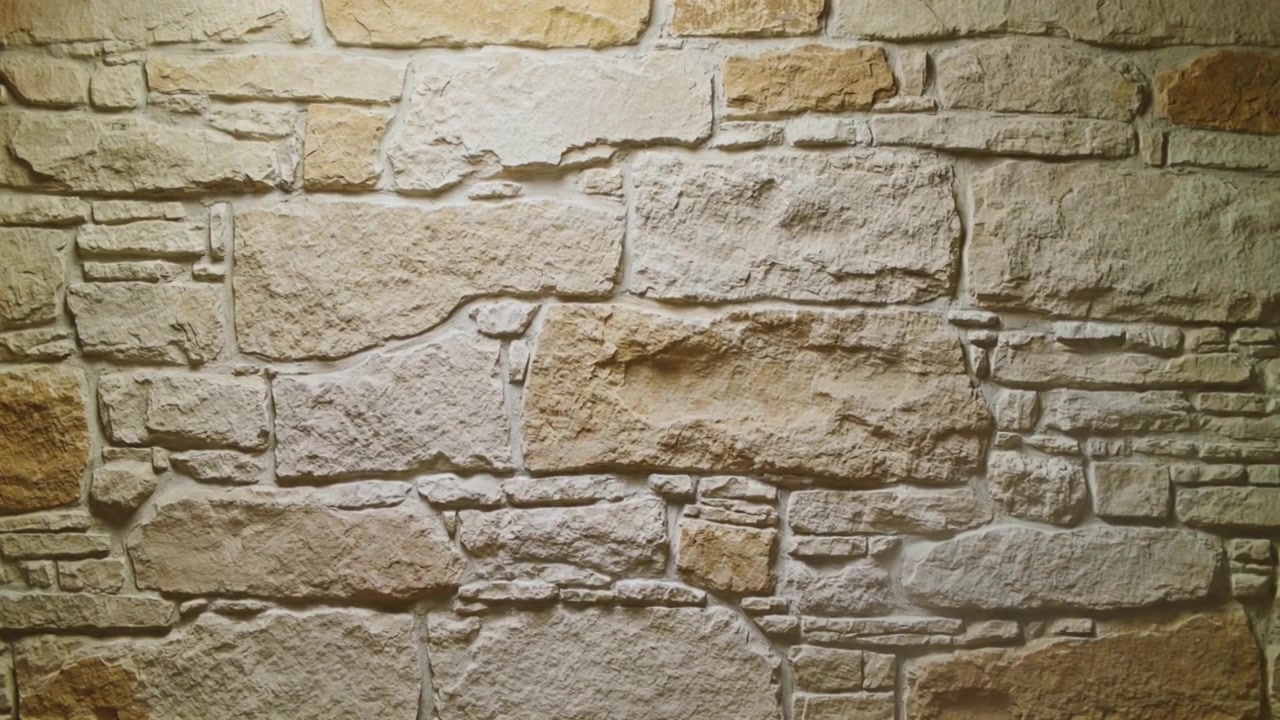 Telecamera fissa che riprende un muro di pietra beige in un corridoio, mostrando una staffa metallica per il controllo della luce.