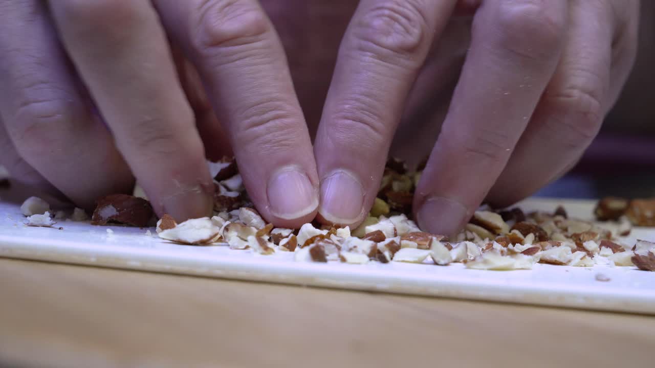 Close-up of a person handling finely chopped almonds during food preparation on a clean white surface