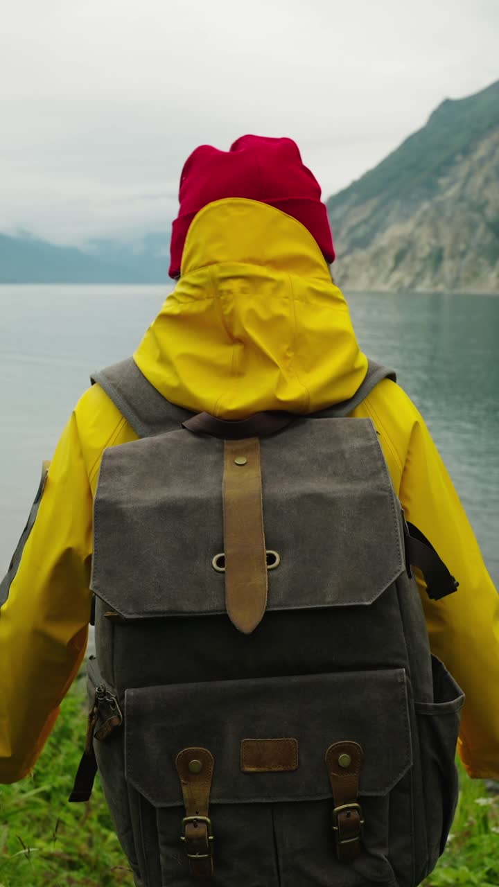 Pendaki Ransel Berjaket Hujan Kuning Melihat Danau dan Pegunungan yang Indah