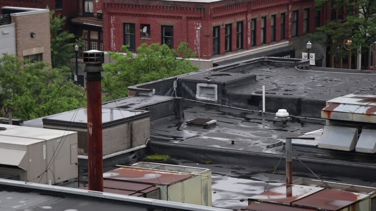 En lo alto de edificios urbanos oxidados con chimeneas, rejillas de HVAC, ventiladores y fondos de ladrillo.